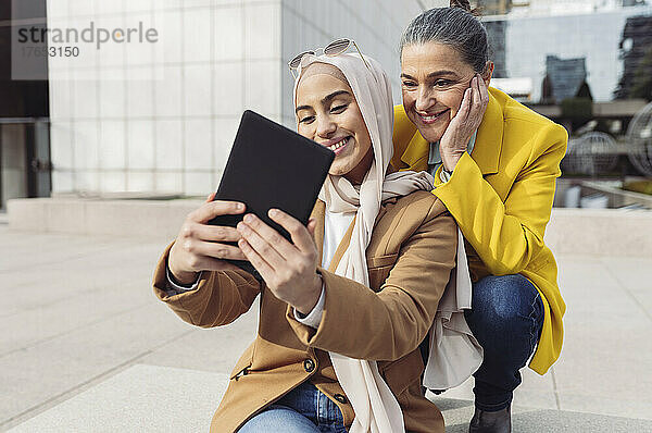 Lächelnde junge Geschäftsfrau  die im Büropark ein Selfie mit einem Kollegen über einen Tablet-PC macht