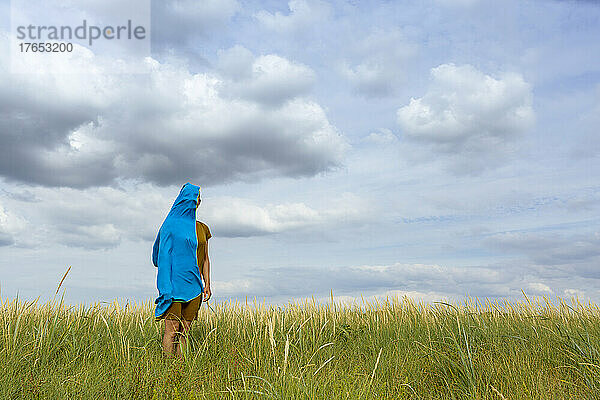 Frau steht inmitten von Gras  das mit einem blauen Schal bedeckt ist  auf einer Wiese