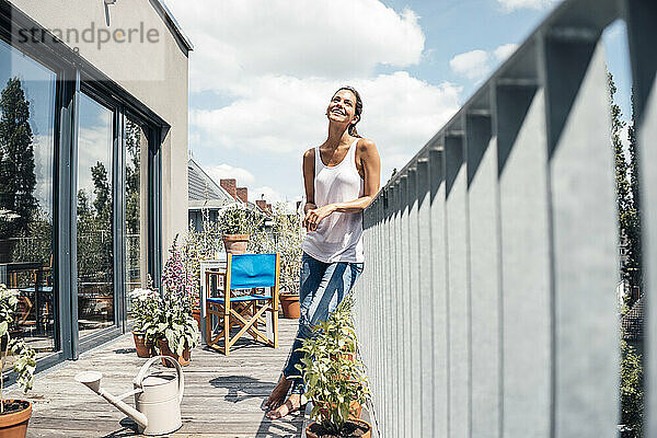Glückliche Frau lehnt an einem sonnigen Tag am Geländer des Balkons