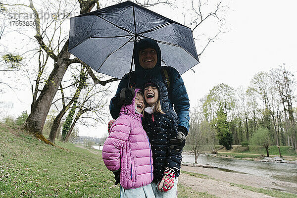 Glücklicher Vater mit Töchtern  die unter einem Regenschirm stehen