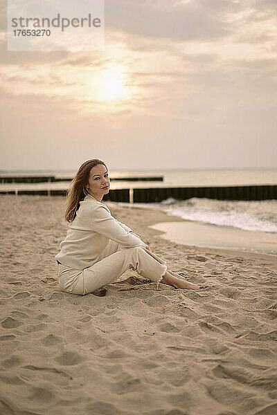 Beautiful woman sitting on sand at sunset