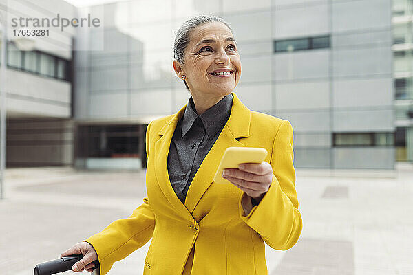 Glückliche Geschäftsfrau mit Smartphone vor modernem Gebäude