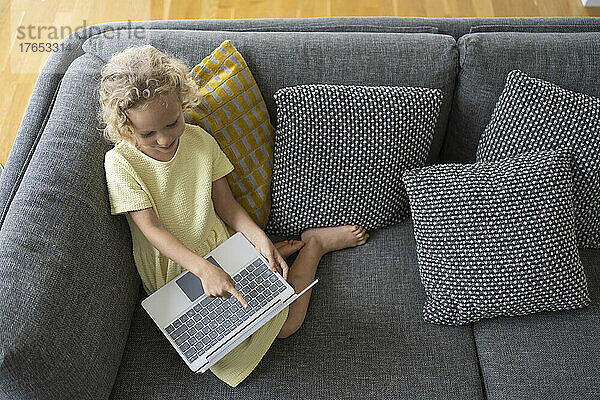 Mädchen mit Laptop sitzt zu Hause auf dem Sofa