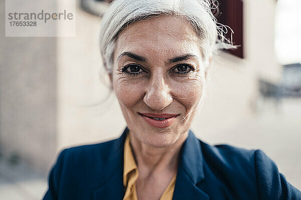 Lächelnde Geschäftsfrau mit grauen Haaren vor Bürogebäude