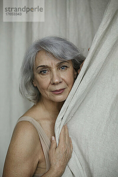 Ältere grauhaarige Frau vor Vorhang zu Hause