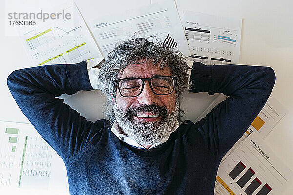 Happy freelancer with eyes closed lying on documents at home