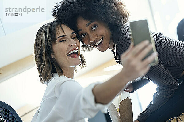 Glückliche Geschäftsfrau  die im Büro ein Selfie mit einem Kollegen per Mobiltelefon macht