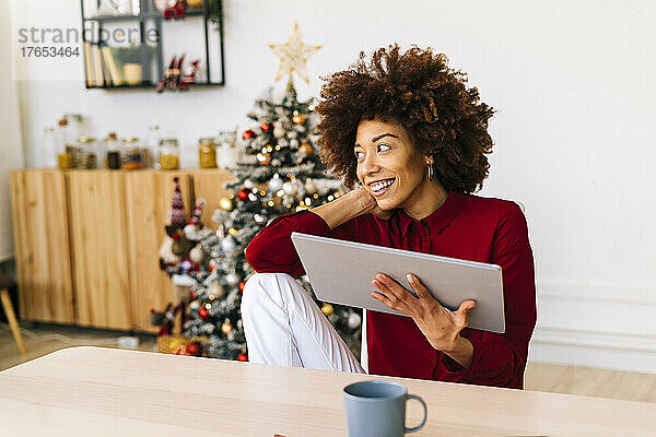 Glückliche Afro-Frau mit Tablet-PC sitzt zu Hause im Wohnzimmer