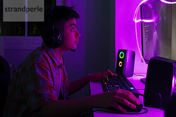 Überraschter Junge mit Kopfhörern  der zu Hause ein Videospiel am Computer spielt