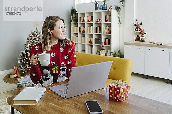 Blonde Frau mit Laptop und Kaffeetasse sitzt am Tisch