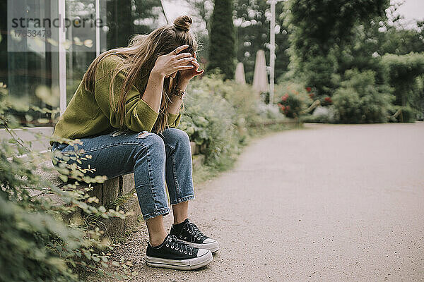 Gestresste Frau mit Kopf in den Händen sitzt an der Wand im Park