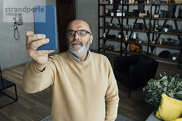 Älterer Mann mit Brille macht zu Hause ein Selfie mit dem Smartphone