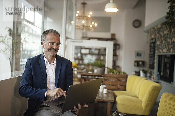 Lächelnder Geschäftsmann benutzt Laptop im Café