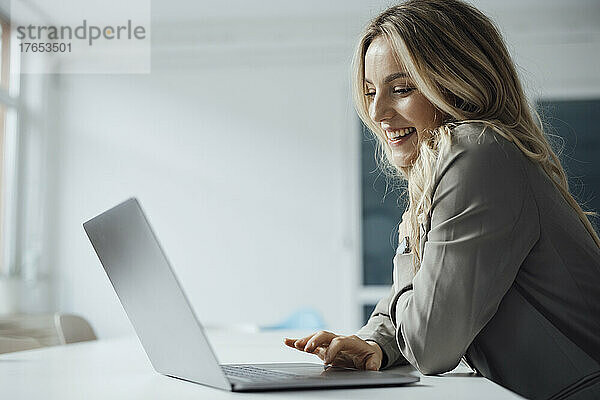 Glückliche Geschäftsfrau  die Laptop am Schreibtisch im Büro benutzt