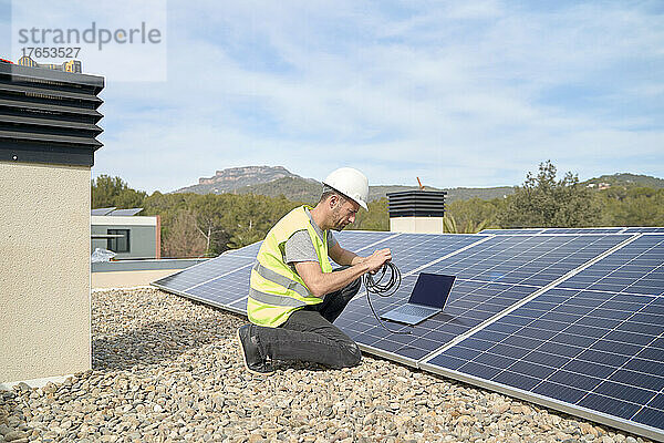 Ingenieur mit Laptop und Kabel installiert Sonnenkollektoren auf dem Dach