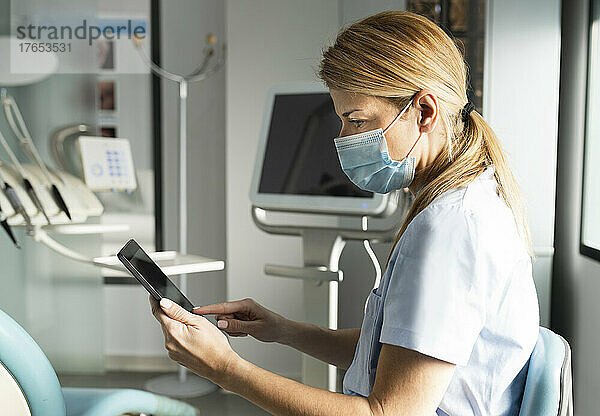 Zahnarzt mit schützender Gesichtsmaske mit Tablet-PC in der Zahnklinik