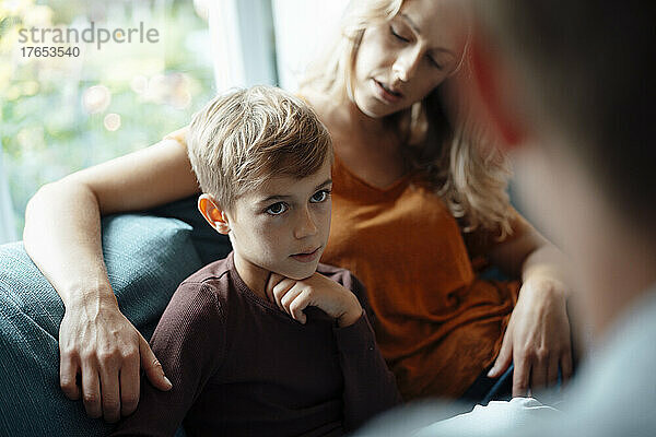 Blonder Junge sitzt neben seiner Mutter und schaut den Mann zu Hause auf dem Sofa an