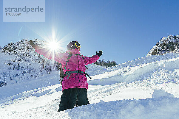 Mann steht an einem sonnigen Tag mit ausgestreckten Armen am schneebedeckten Berg