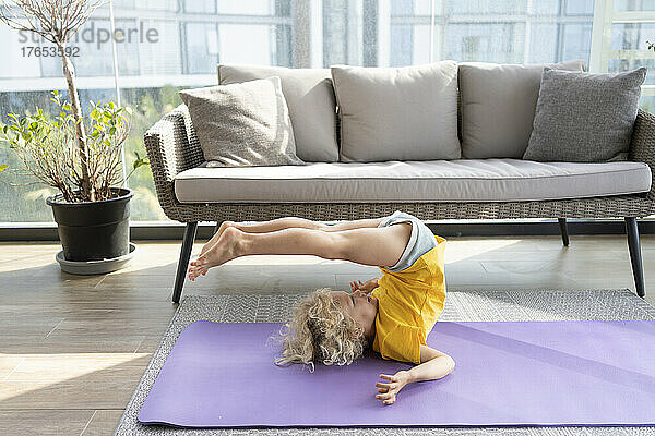 Lächelndes Mädchen  das zu Hause vor dem Sofa Yoga praktiziert