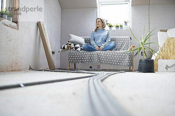 Nachdenkliche Frau sitzt auf Sofa im Dachboden