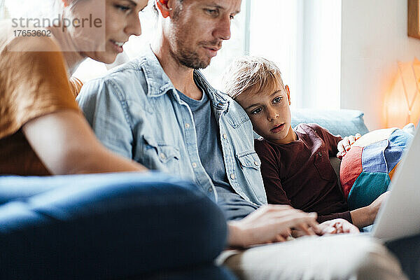 Mann und Frau teilen sich Laptop und sitzen zu Hause neben ihrem Sohn im Wohnzimmer