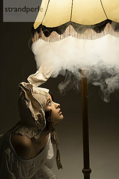 Neugierige junge Frau mit Hasenohren blickt in die rauchige Lampe