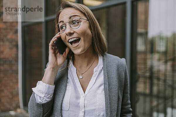 Glückliche Frau  die vor dem Gebäude mit dem Handy telefoniert