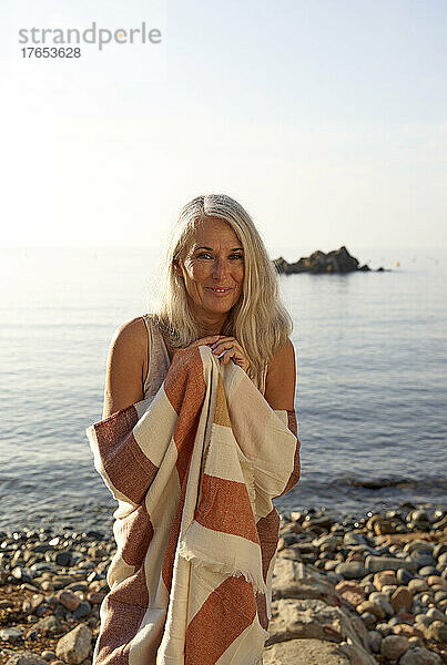 Lächelnde Frau  in einen Schal gehüllt  am Strand