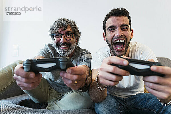 Fröhlicher Vater spielt zu Hause Videospiel mit Sohn