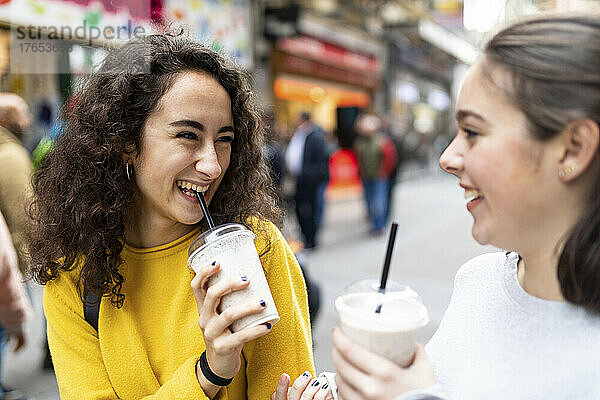 Glückliche junge Frau schaut einem Freund zu  der Milchshake trinkt