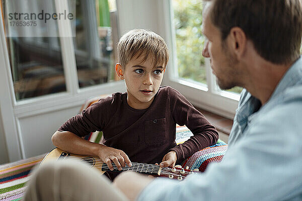 Blonder Junge mit Gitarre spricht zu Hause mit Vater