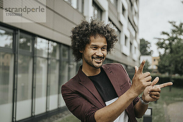 Happy man with curly hair gesturing in front of building