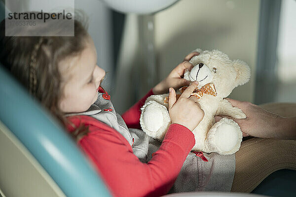 Kleines Mädchen sitzt mit Stofftier auf einem Zahnarztstuhl in einer medizinischen Klinik