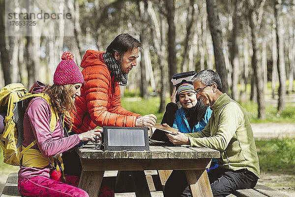 Reife Männer diskutieren über Tagebuch mit Frauen  die am Picknicktisch im Wald sitzen
