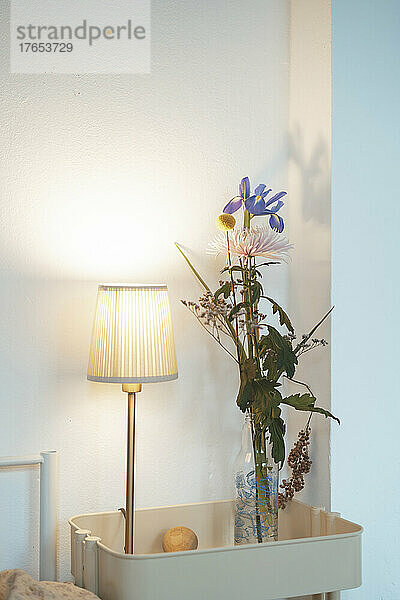 Blumenvase und beleuchtete Lampe vor der Wand zu Hause