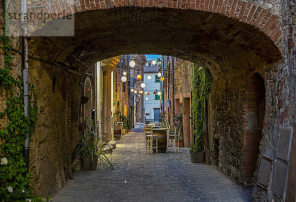 Italien  Provinz Siena  Radicondoli  Laternen beleuchten die Gasse der Altstadt mit Backsteinbogen im Vordergrund