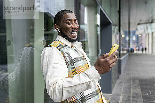 Glücklicher Mann  der mit seinem Smartphone vor einer Glaswand im Internet surft
