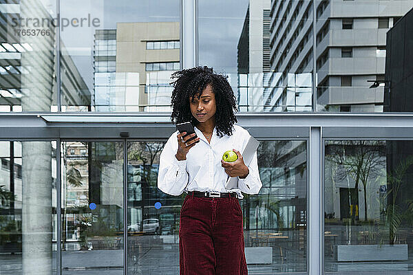 Geschäftsfrau mit lockigem Haar benutzt Mobiltelefon im Büropark