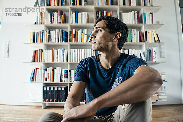 Young man sitting in front of bookshelf at home
