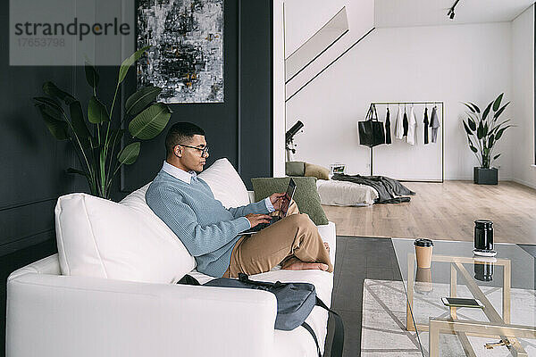 Freiberufler mit Brille und Laptop sitzt zu Hause auf dem Sofa
