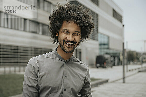 Happy young man with curly hair in front of modern building