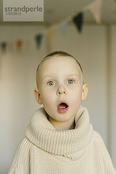 Überraschter Junge mit offenem Mund im Rollkragenpullover zu Hause