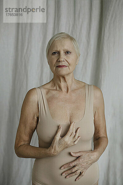 Ältere Frau im Bodysuit steht zu Hause vor dem Vorhang
