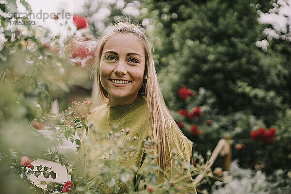 Lächelnde schöne Frau  die neben Rosenpflanzen steht