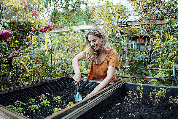 Lächelnde blonde Frau mit Schaufel bei der Gartenarbeit im Hinterhof