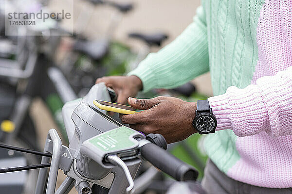 Hand eines Mannes  der am Parkplatz per Mobiltelefon ein Fahrrad mietet