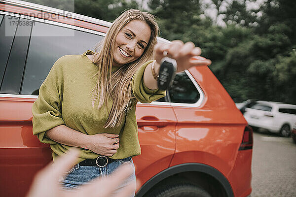 Glückliche junge Frau übergibt Autoschlüssel an Freundin auf Parkplatz