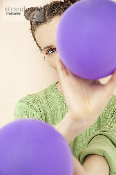 Frau bedeckt Gesicht mit lila Luftballon vor pfirsichfarbenem Hintergrund