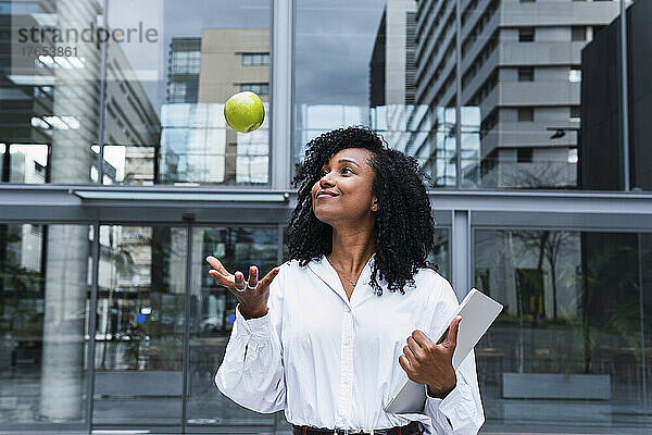 Lächelnde Geschäftsfrau  die im Büropark einen Apfel fängt