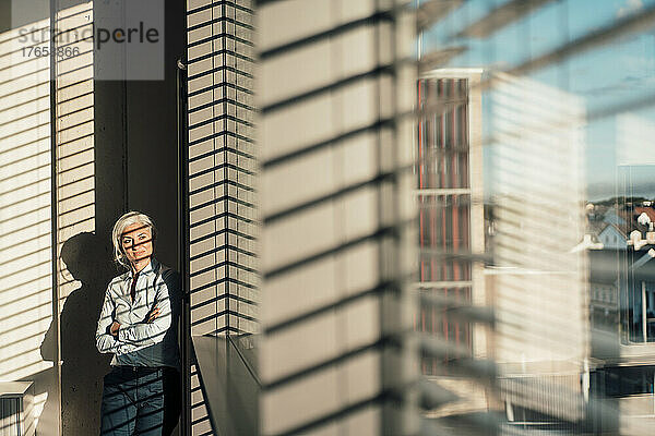 Businesswoman with arms crossed looking through glass window in office